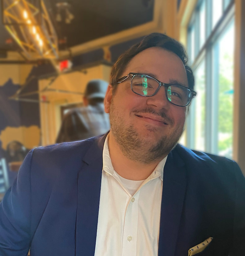 Picture of Greg Siekman smiling, wearing a white dress shirt and blue blazer